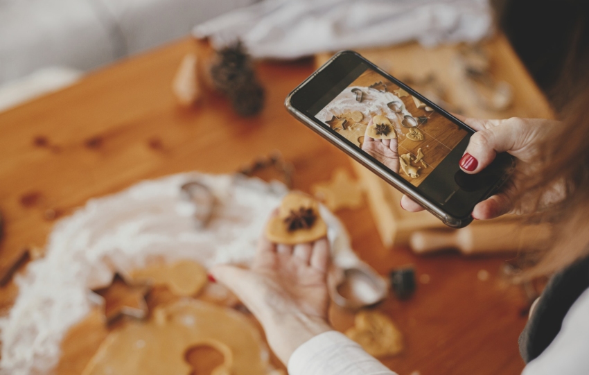 Woman holding phone and taking photo of gingerbread christmas cookies. Instagram photo