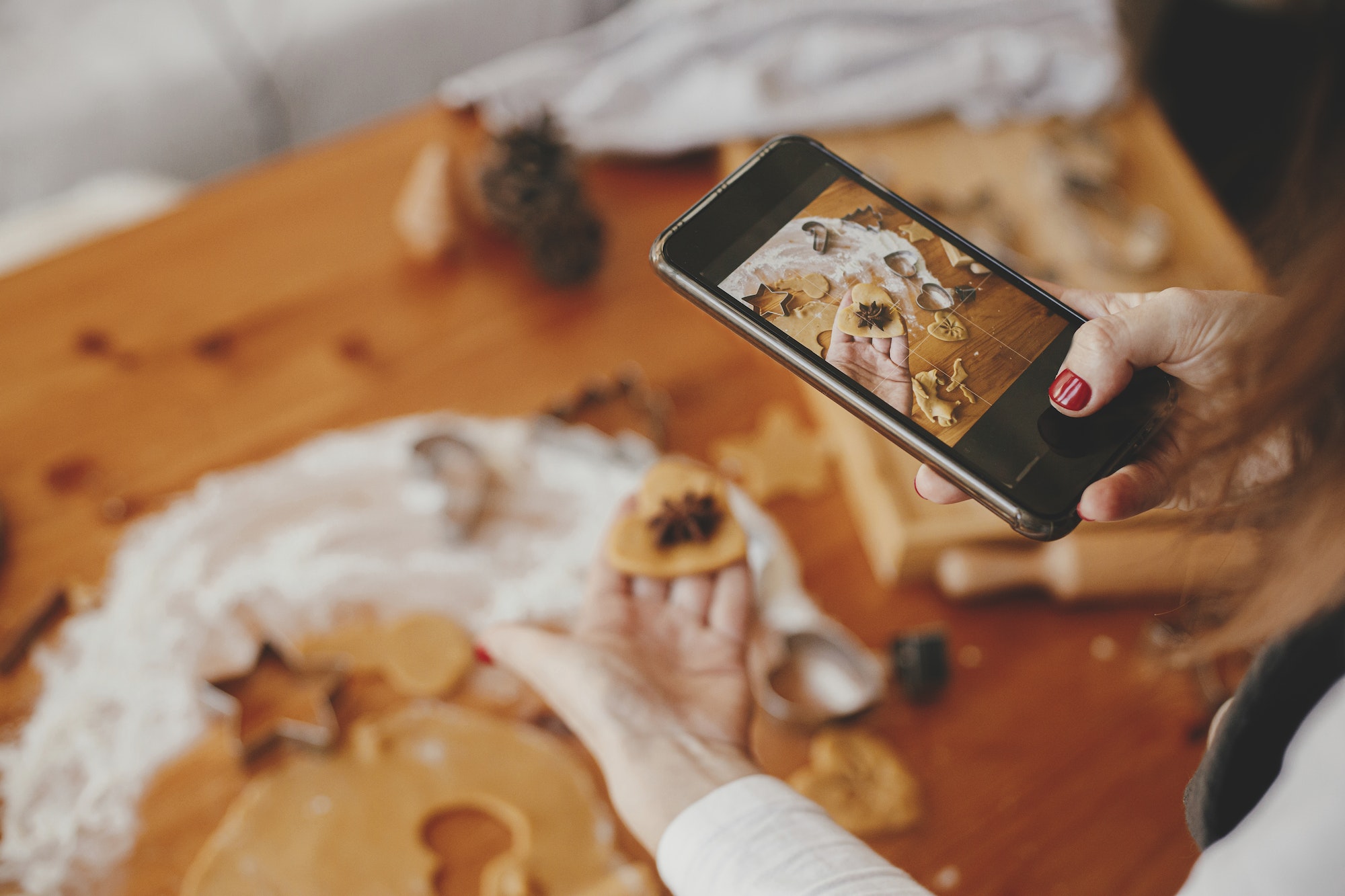 Woman holding phone and taking photo of gingerbread christmas cookies. Instagram photo